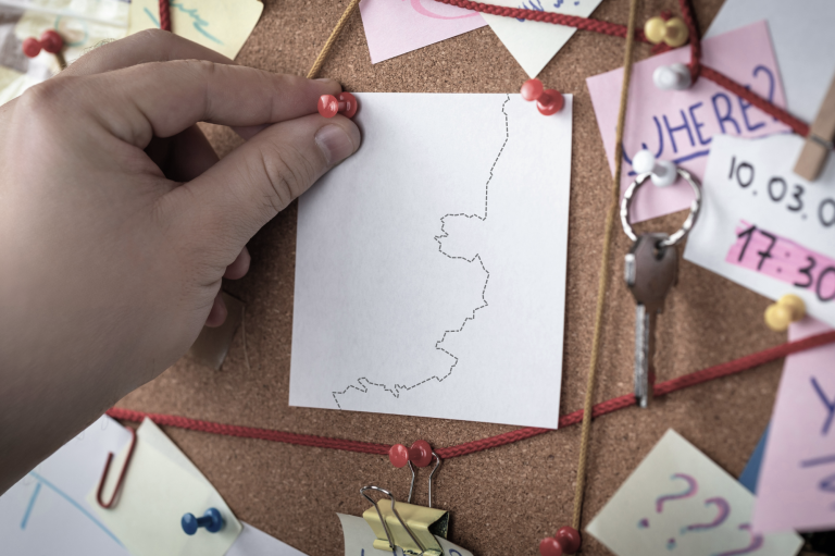 Ausschnitt einer Pinnwand, wie in einem Detektivbüro. Es sind Notizzettel, Verbindungen und Pins zu erkennen. 